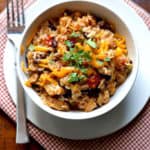 Chicken, Black Bean, and Rice Burrito Bowls in white bowl topped with cheese and chopped cilantro. A fork sits beside the bowl.