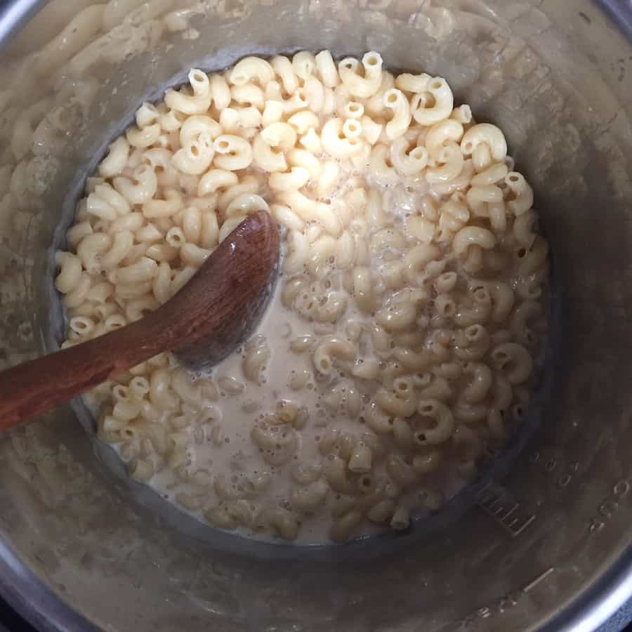 Cooked macaroni in pressure cooker pot with milk added. A wooden spoon stirs the mixture.