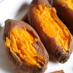 Three cooked sweet potatoes on a platter with cinnamon sicks.