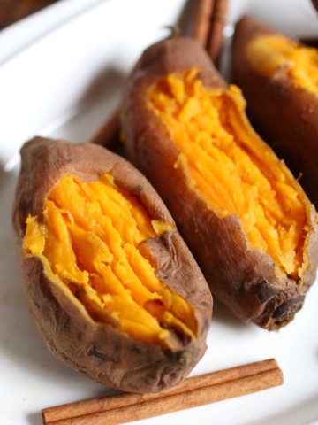 Three cooked sweet potatoes on a platter with cinnamon sicks.