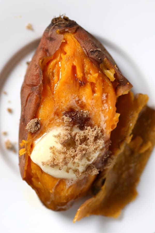 Sweet potato topped with butter and brown sugar on white plate.