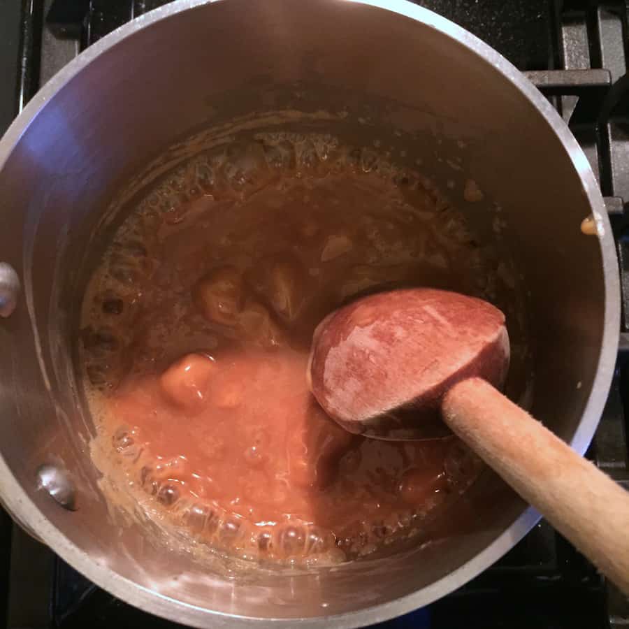 Stirring melting caramel candies with a wooden spoon.