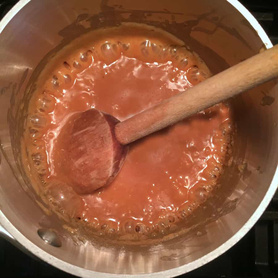 Caramel sauce bubbling in a sauce pan. Wooden spoon stirs the sauce.