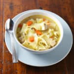 Pressure cooker chicken soup in a white bowl with a spoon beside it.