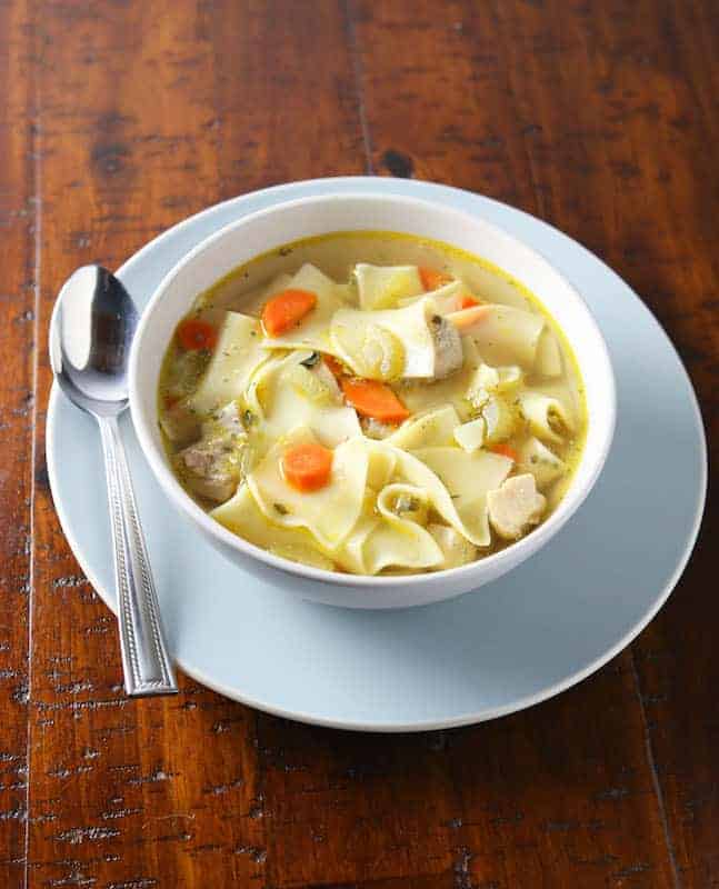 Pressure cooker chicken soup in a white bowl with a spoon beside it.