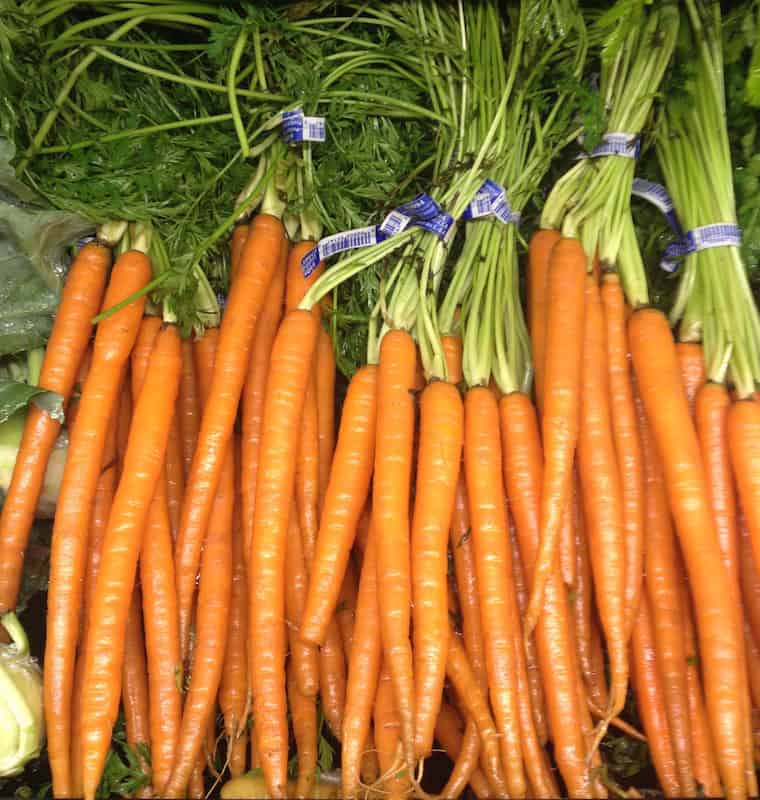 Carrots with steams attached on grocery store shelf.