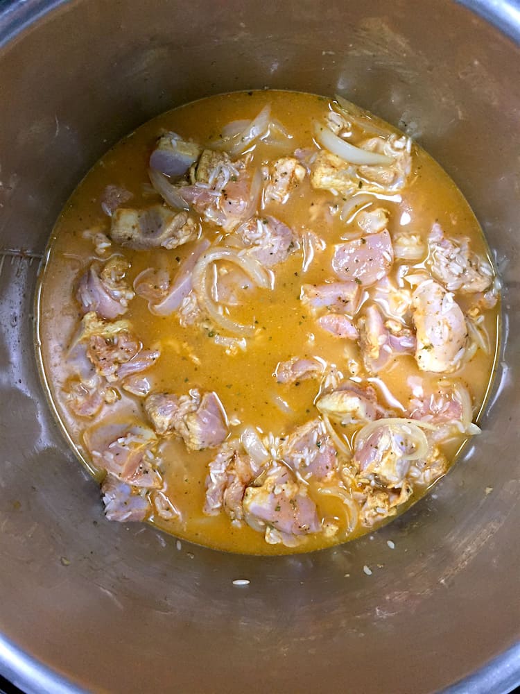 Raw chicken with rice and onions in broth a pressure cooker pot.