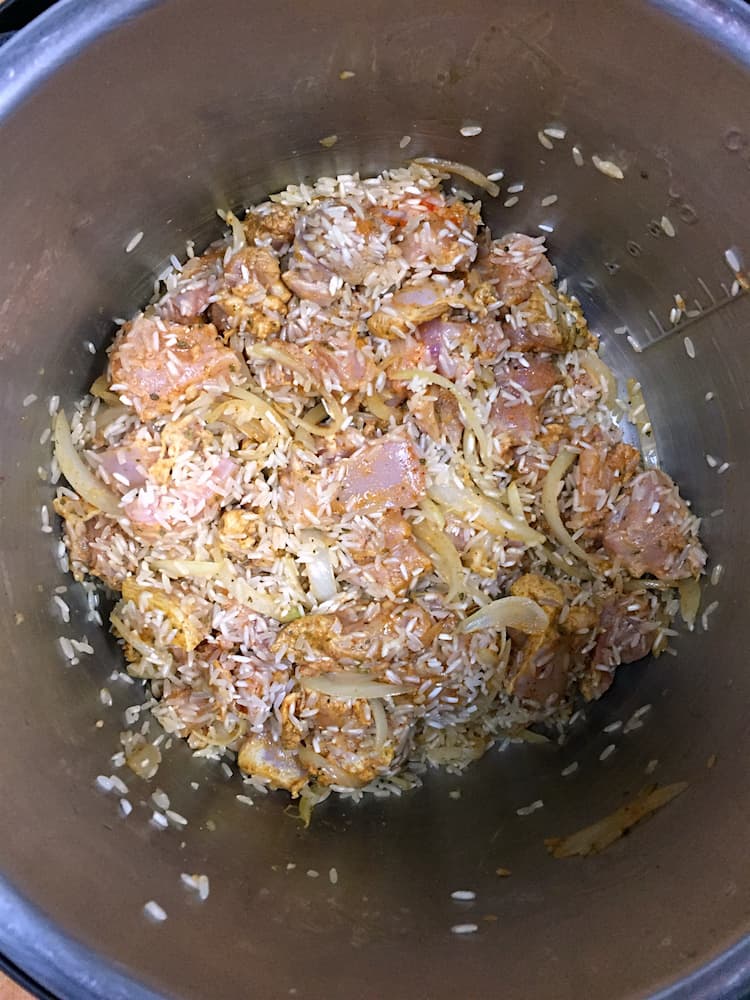 Raw chicken with rice and onions in a pressure cooker pot.