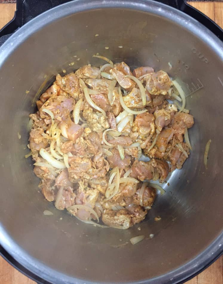 Cubes of raw chick and onions cooking in a pressure cooker pot.