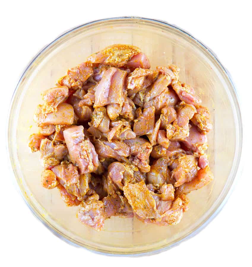 Marinating cubes of raw chicken in a glass bowl.