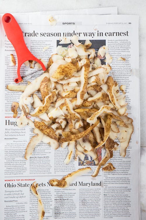 Potato peels and red peeler on newspaper. 