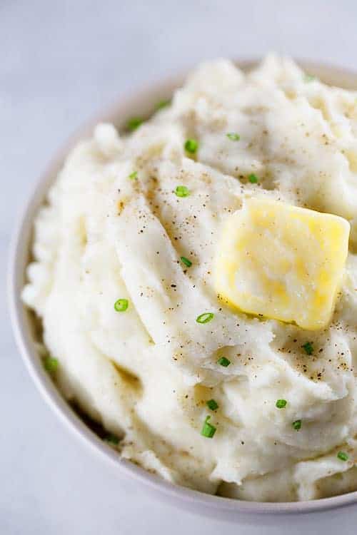 Bowl of mashed potatoes with butter, black pepper and chives on top.