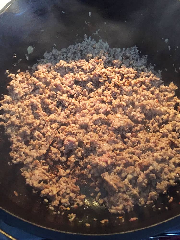 Cooked, crumbled sausage in a cast iron pot. 