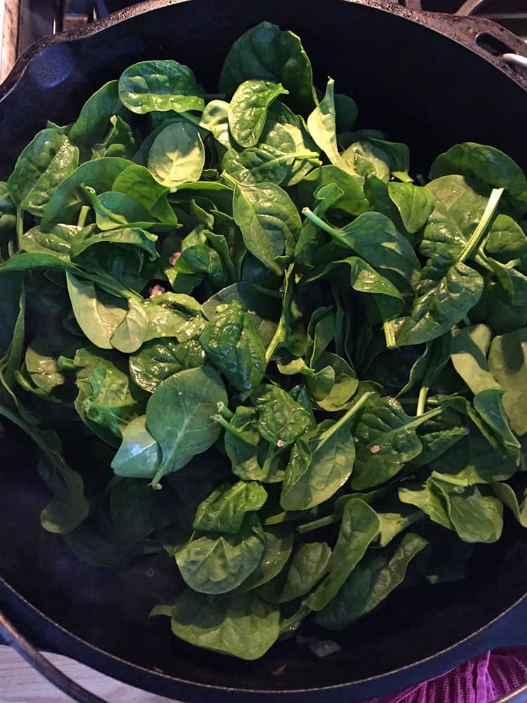 Raw spinach added to the pot of cooked sausage. 