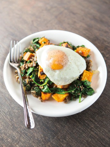 Egg cooked over-medium sits atop sweet potato hash with spinach and sausage.