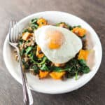 Over medium egg sits atop a plate of sweet potato hash with spinach and sausage.