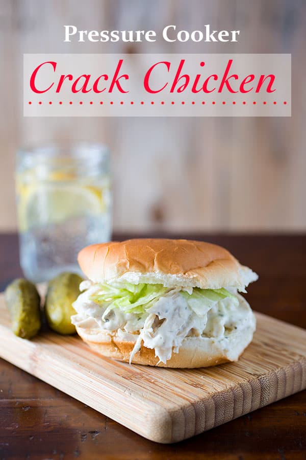 Crack chicken on a bun with shredded lettuce. In the background, a pickle and glass of lemonade. Text on image: Pressure Cooker Crack Chicken.