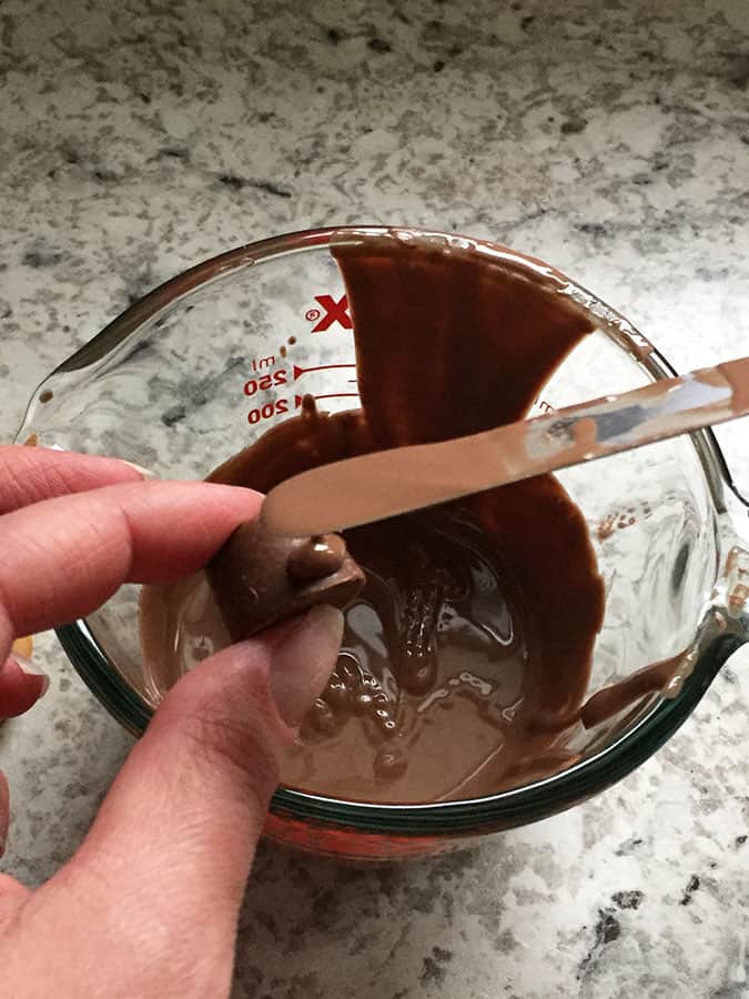 A hand holds Rolo candy while adding a drop of melted chocolate with a metal spatula.