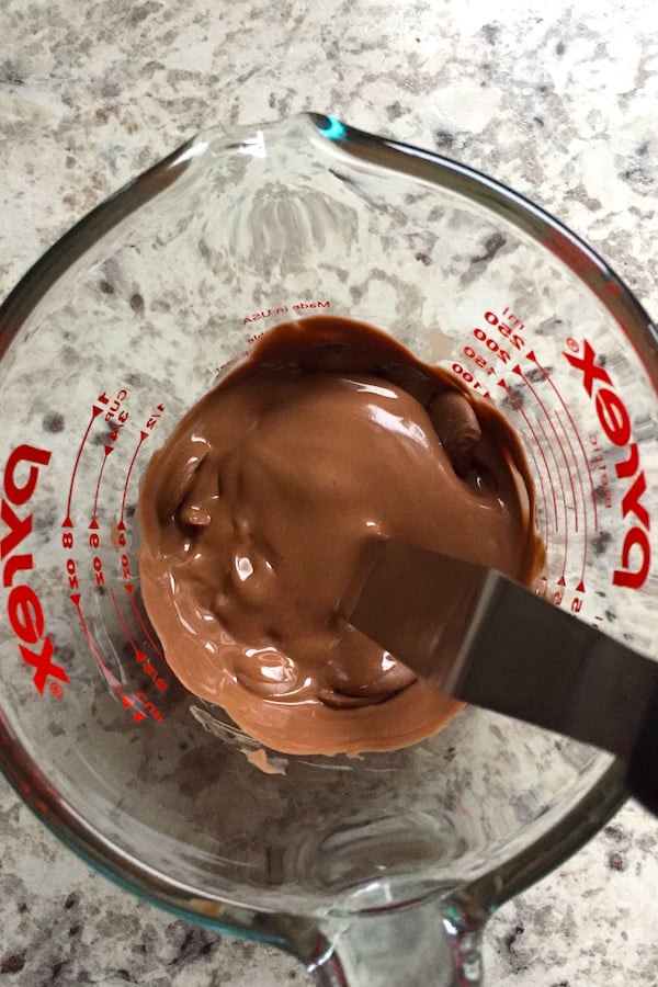 Melted chocolate in a measuring cup. A few lumps of chocolate remain.