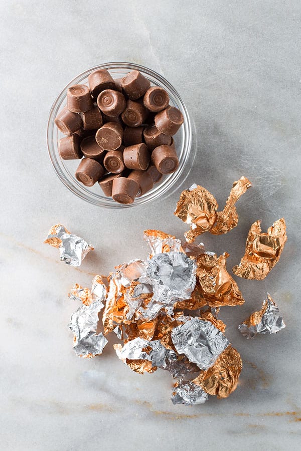 Unwrapped Rolo candies in a bowl. The wrappers sit below the bowl.