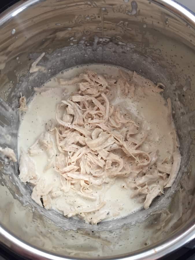 Shredded chicken in pressure cooker pot with melted cream cheese sauce.