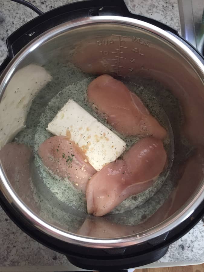 Raw chicken, cream cheese, water, and ranch dressing mix in a pressure cooker pot.