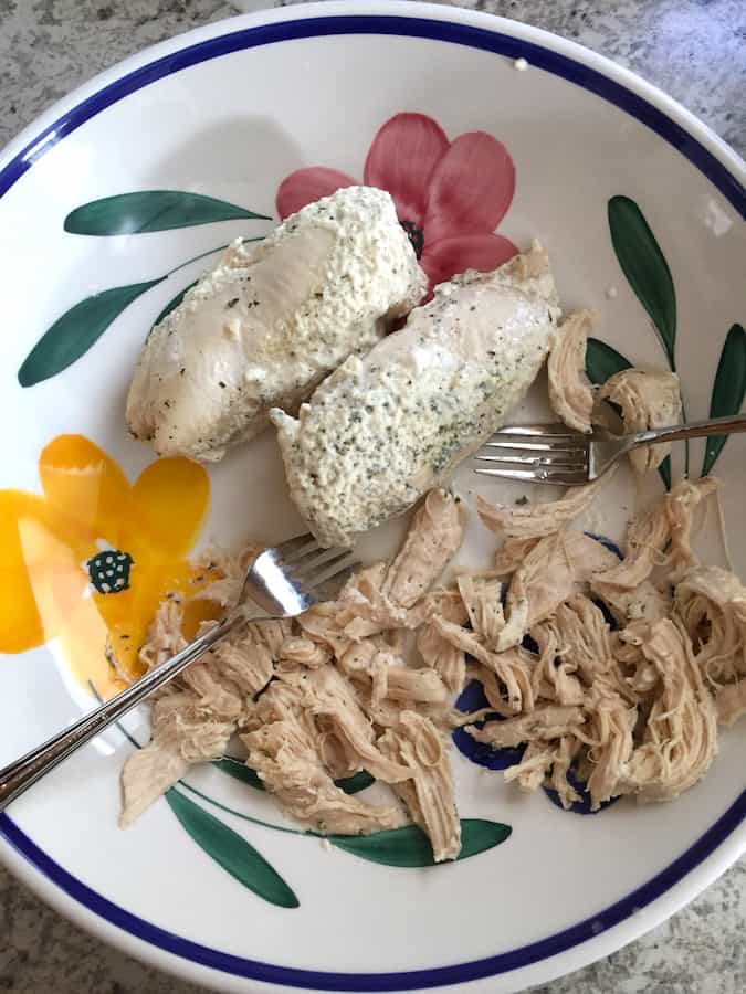 Cooked chicken breast in a large bowl being shredded with two forks.