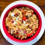 Beer can chicken with rice in a red bowl. Pieces of cooked chicken and bacon are on top of the cooked rice.