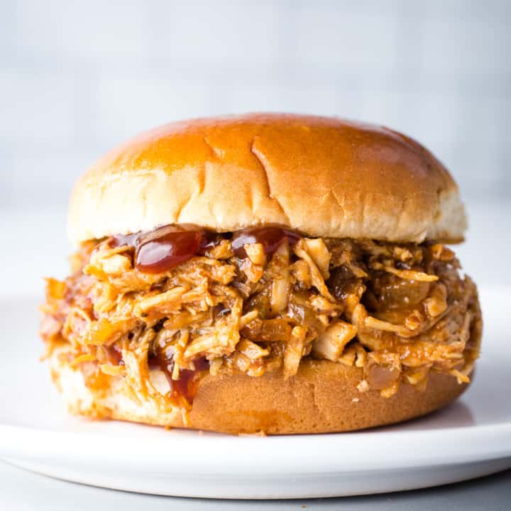 Pulled chicken sandwich on a bun served on a white plate.
