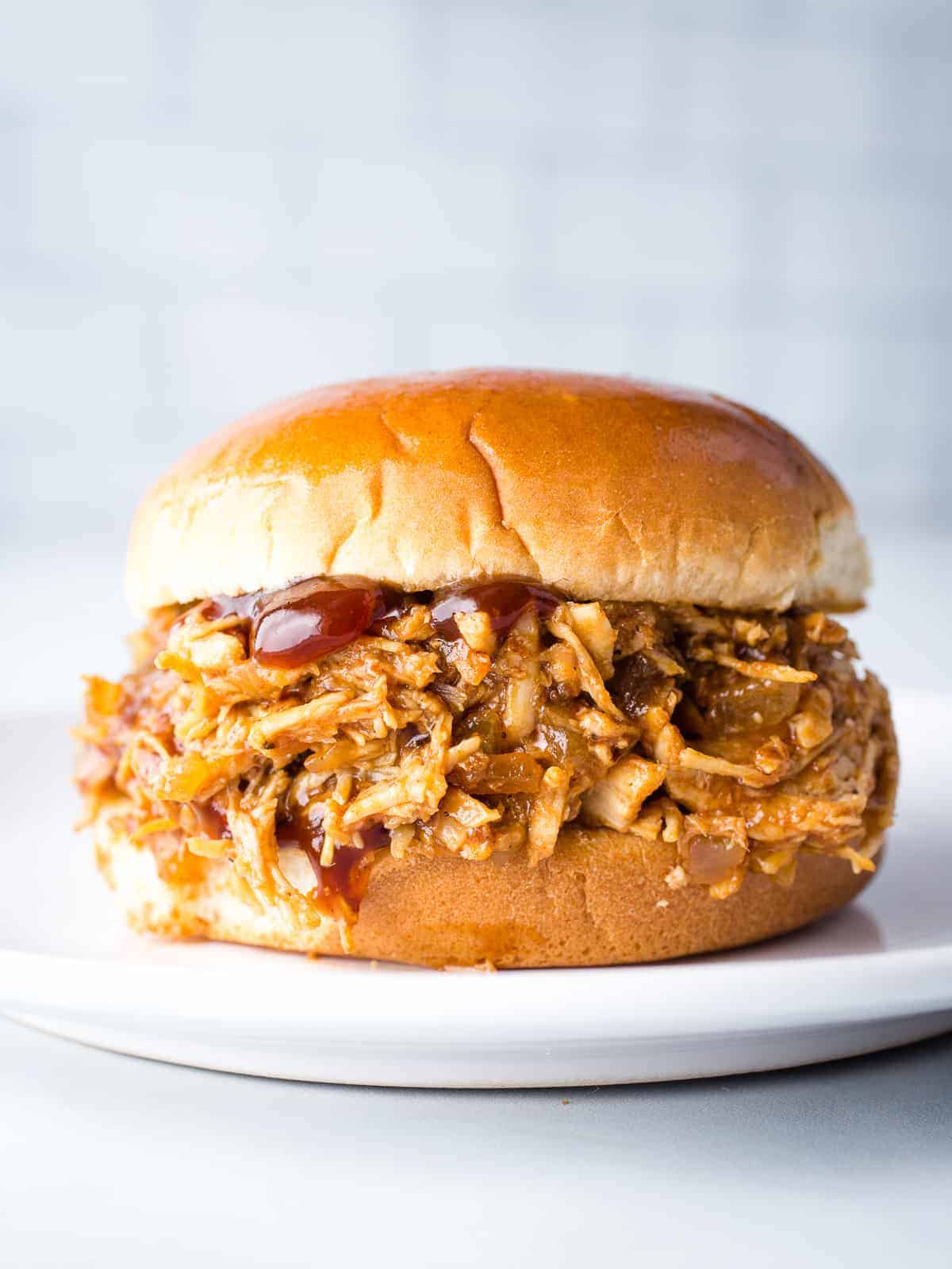 Pulled chicken sandwich on a bun served on a white plate.
