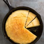 Skillet cornbread in pan. Two pieces are sliced.