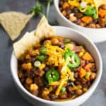 Two bowls with chili topped with grated cheese and jalapeño slices.