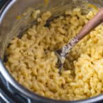 Creamy Instant Pot macaroni and cheese being stirred by a wooden spoon.