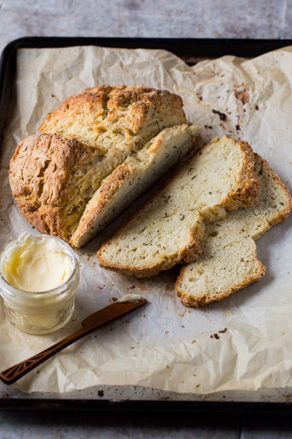 Irish soda bread with caraway seeds on baking sheet. A bowl of butter sits alongside.