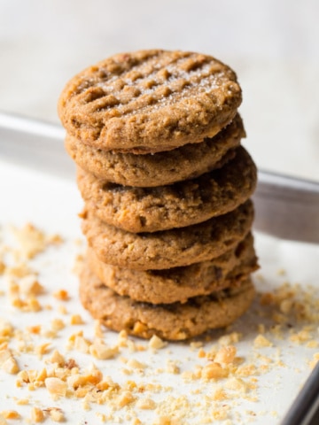 Stack of peanut butter cookies. Top is sprinkled with granulated sugar. Chopped peanuts are scattered around the cookies.