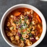 Bowl of Pasta e fagioli on gray counter. Topped with chopped herbs and grated parmesan.