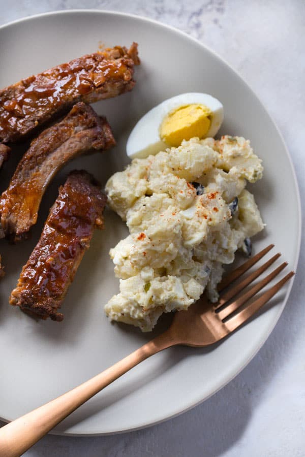 Potato salad on plate with ribs and a hard boiled egg on the side.