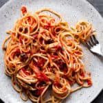 Pasta with tomatoes and olives in a gray speckled plate.