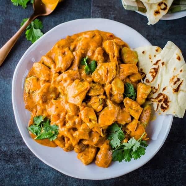 Butter chicken on a plate with naan on the side.