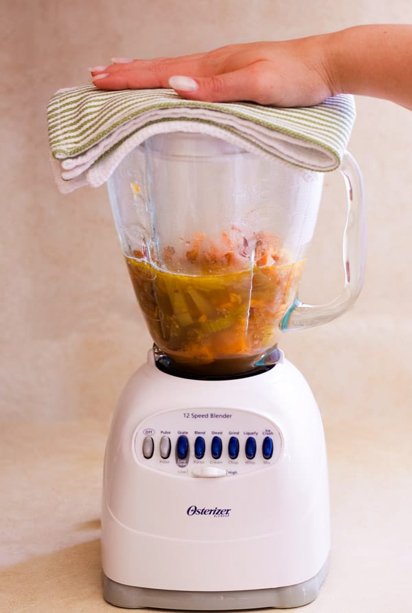 Blender with soup. A hand hold the lid on the blender. 