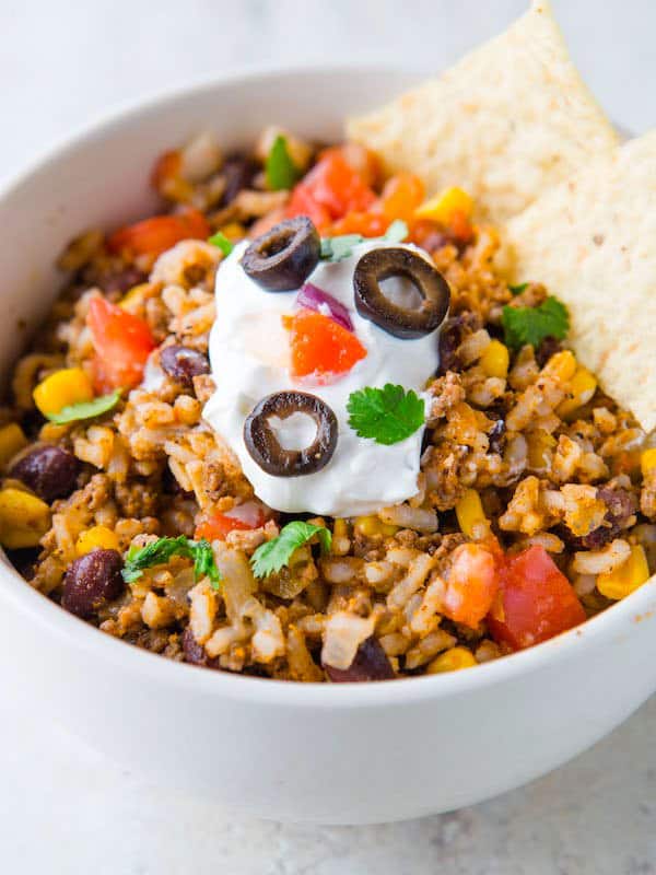 White bowl filled with cooked rice, black beans, corn, and ground beef. Topped with sour cream and salsa.
