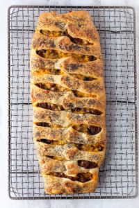 Baked ground beef Stromboli on wire rack. The stromboli is topped with poppy seeds.