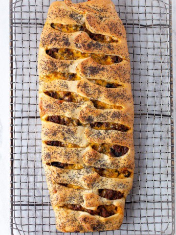 Baked ground beef Stromboli on wire rack. The stromboli is topped with poppy seeds.