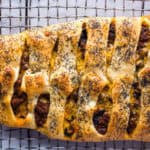 Overhead shot of a baked stromboli topped with poppy seeds. Filling, which includes ground beef and cheese, is exposed between the strips of dough.