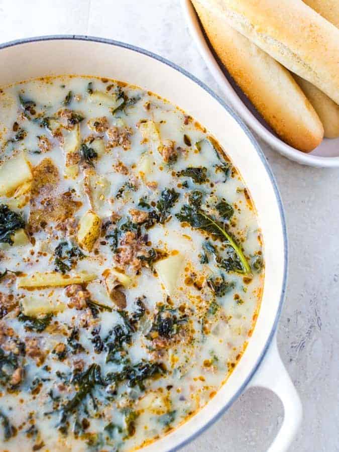 Pot of zuppa toscana soup. Breadsticks in upper right corner. 