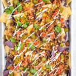 Sheet Pan with Baked Nachos. Topped with Cooked Ground Beef, Corn, Salsa, Drizzled Sour Cream, Beans, and Chopped Cilantro.