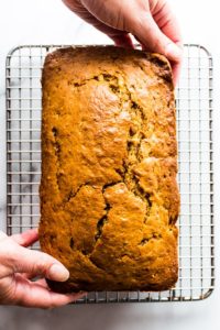 Hands place a brown sugar banana bread onto a cooling rack.