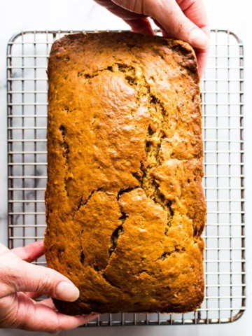 Hands place a brown sugar banana bread onto a cooling rack.