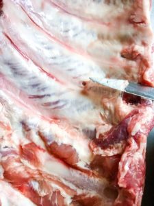 Point of knife under the silverskin of a rack of baby back ribs.