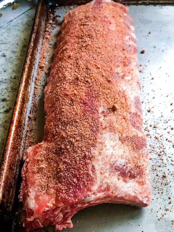 Baby back rib on a sheet pan sprinkled with a spice rub.